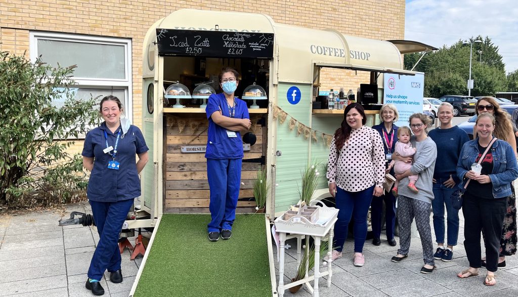 Maternity staff in blue uniforms pictured outside Lister Hospital's Diamond Jubilee Maternity Unit with members of the Lister MVP, with a coffee shop van behind.