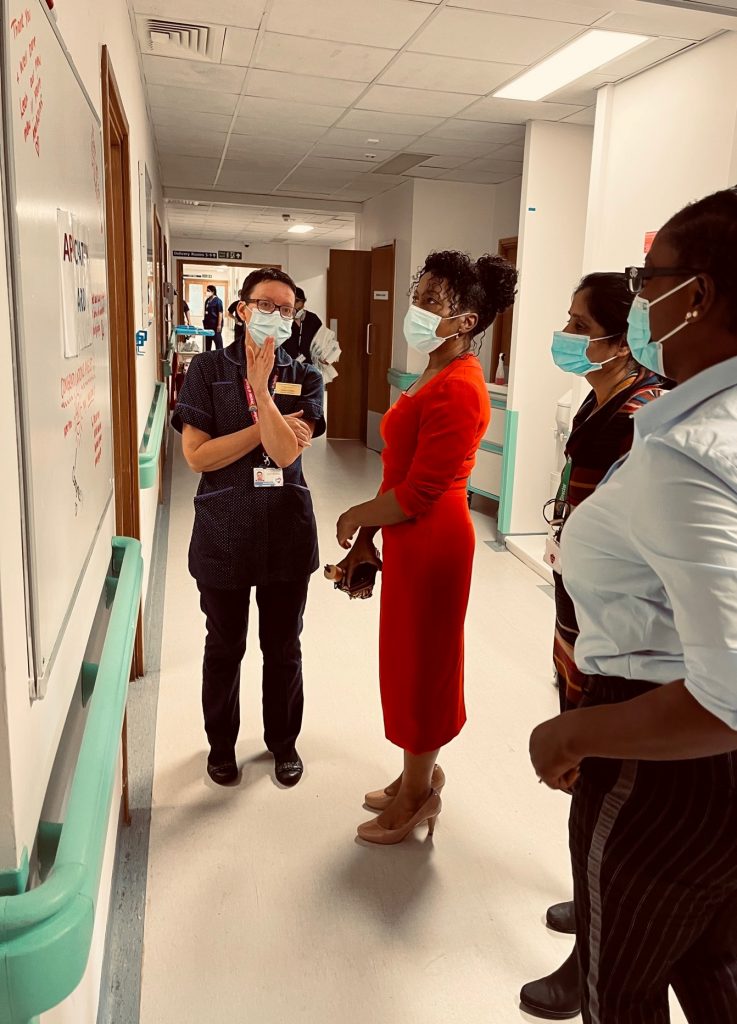 Katie Chilton gesturing to England’s chief midwifery officer Professor Jacqueline Dunkley-Bent, wearing a red dress, on the maternity unit at Lister as a colleague and Wendy Olayiwola, the national maternity lead for equality at NHS England and Improvement, look on. 