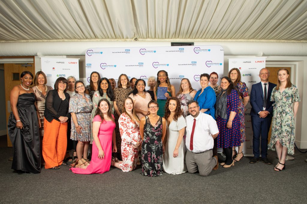 Lots of staff from the maternity and obstetrics & gynaecology teams in colourful outfits with their award, against a white backdrop with sponsors logos.