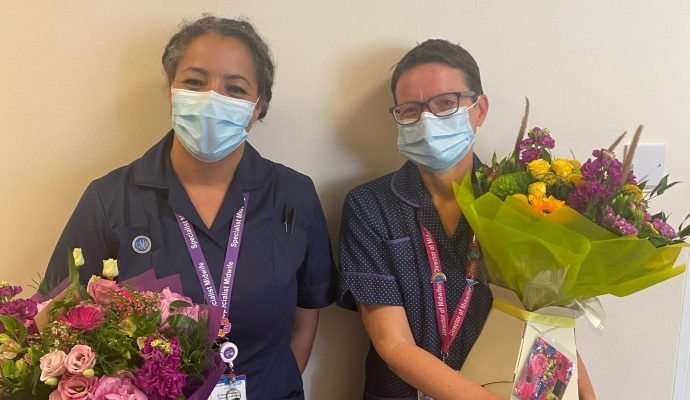 Multiple pregnancy specialist midwife Dionne Thompson and Katie Chilton, East and North Hertfordshire NHS Trust’s director of midwifery, both wearing their blue uniforms and holding bouquets of colourful flowers after receiving national awards.