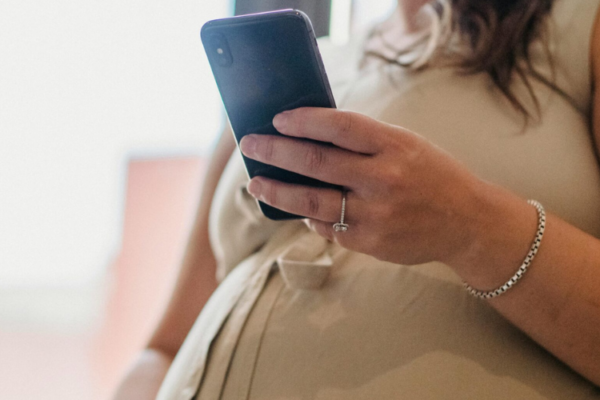 An image taken of a pregnant woman. she is pictured looking at her mobile phone.