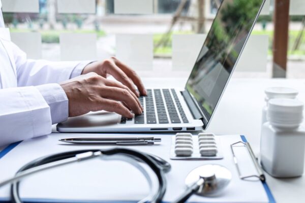 A stethoscope, a clipboard, and a laptop with a man's hands typing