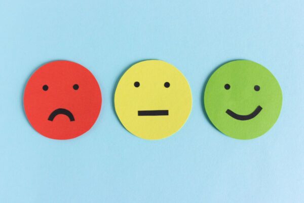 On a blue background, three drawings of faces; a red sad face, a yellow neutral face, and a green happy face.