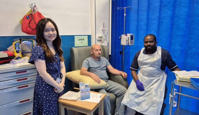 Two members of staff from the clinical team are with a patient who is seated in hospital about to have an immunotherapy injection for cancer treatment.
