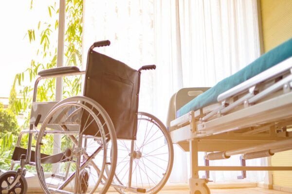 A wheelchair and hospital bed sit before a sunny window