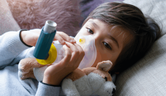 A child photographed breathing in an inhaler via a spacer device.