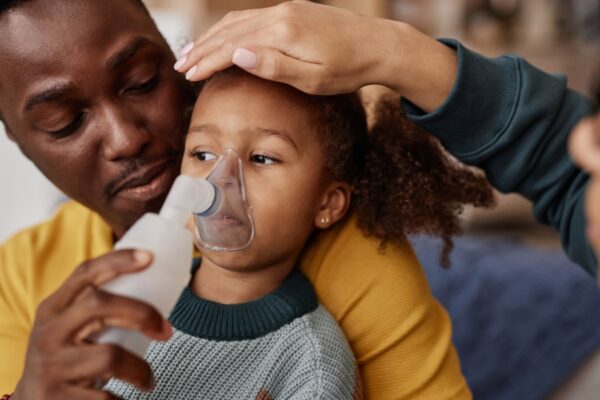 Black father with young daughter using a nebuliser