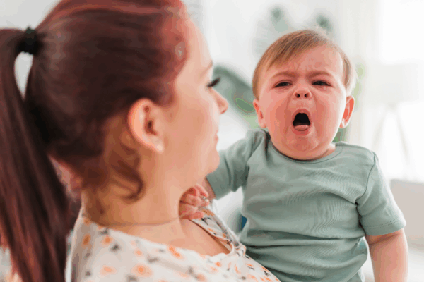 White mother holding a coughing baby.