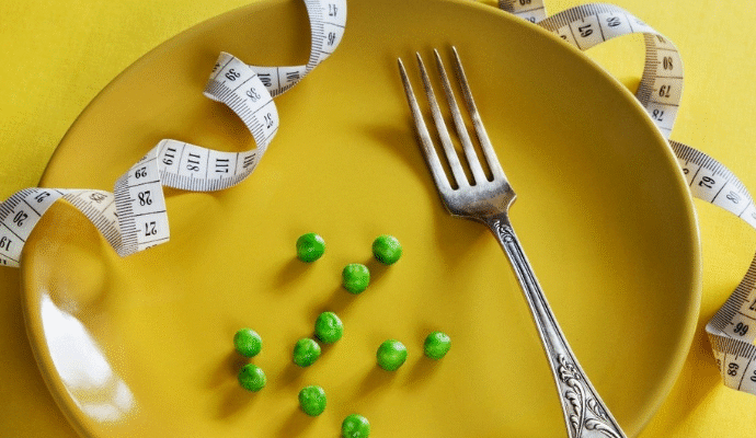 A royalty-free image of a yellow plate with just 11 peas and a single fork on it. Around the plate is a measuring tape.