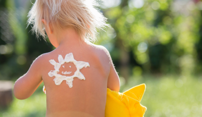 A royalty-free photo of a child playing outside. They are topless with a sun drawing on their back, made out of suncream.