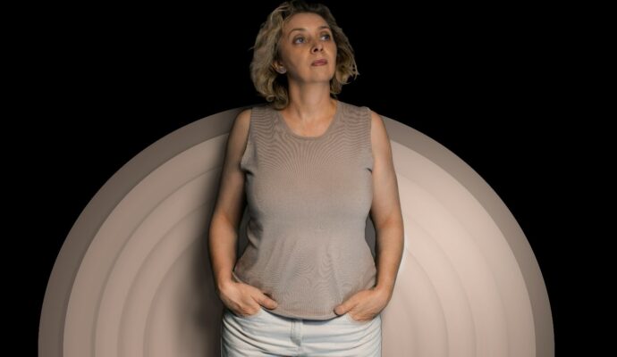 A woman in her mid-to-late 50s posing for a photograph on a black background with cream circles.