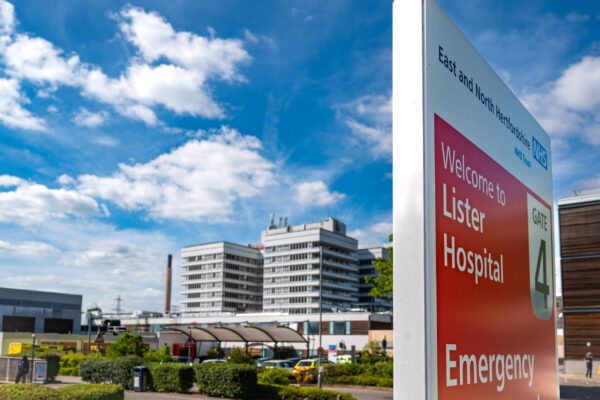 A picture taken outside on a sunny day. Photographed is part of Lister Hospital below blue skies. A sign in the foreground says "Welcome to Lister Hospital."